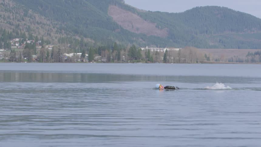 A person swimming in a wetsuit and goggles in a lake