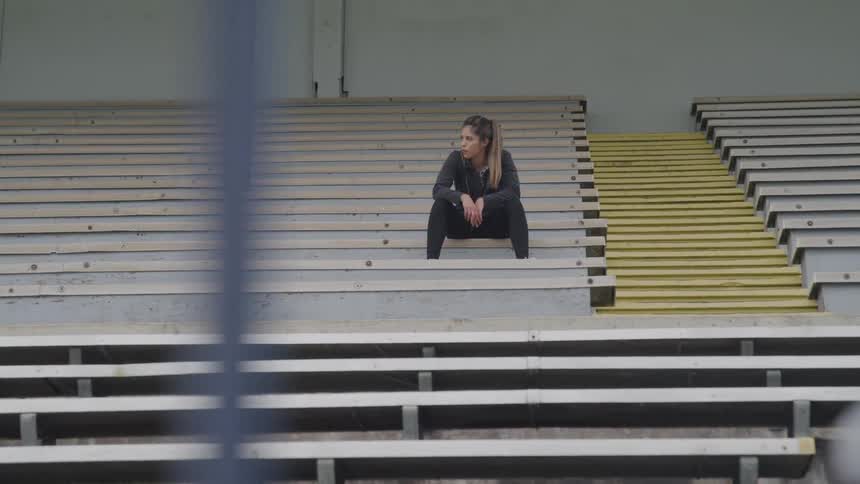 A woman sits in the stands of an empty stadium with her arms resting on her knees