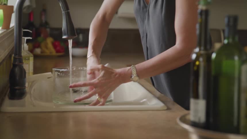 Woman standing at the sink in her kitchen washes out a clear glass bowl and looks up to glance out the window