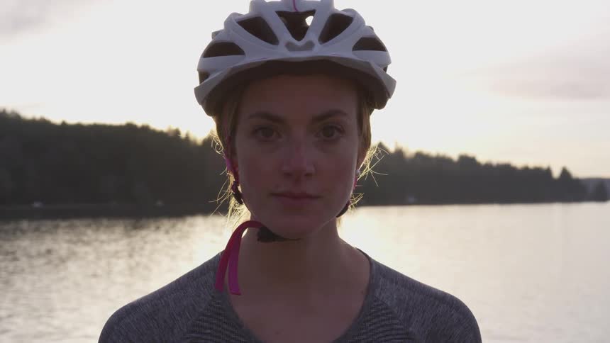 Woman in biking helmet stands in front of lake with forest in background