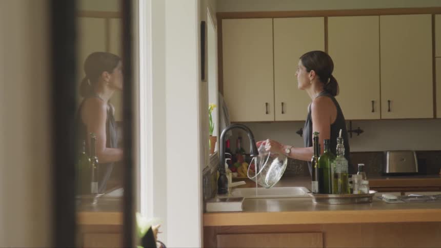 A white woman rinses out a glass container at a kitchen sink