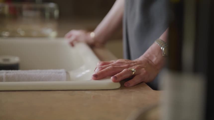 Woman stands in front of kitchen sink putting her hands on during daylight
