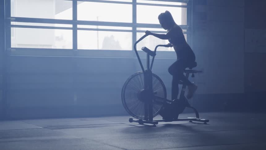 Silhouette of a woman working out on a stationary bike with a large wheel