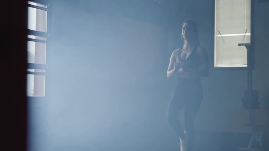 A woman does step ups with a knee raise in a workout room near windows