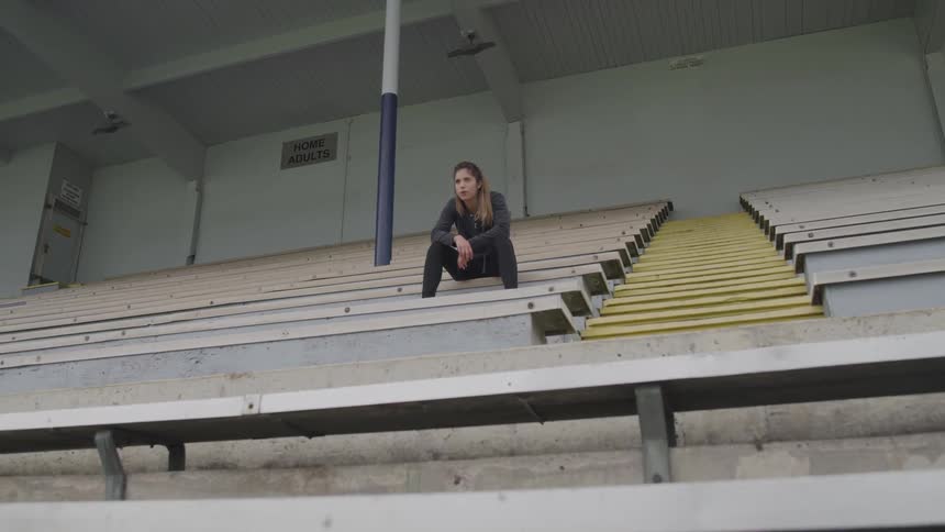 A woman in workout clothing rests in the bleachers