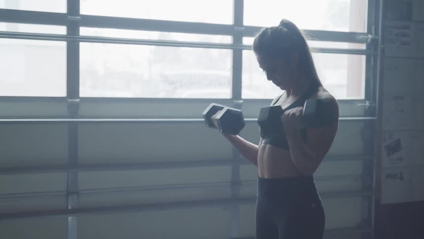 A young white woman lifts dumbbells