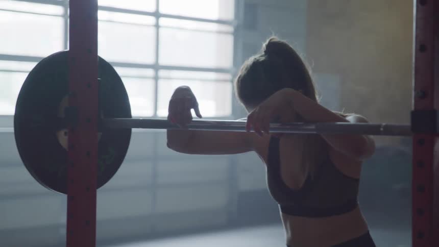 A young white woman leans on a barbell in a gym