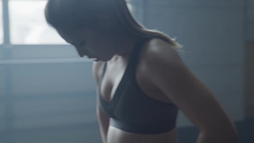 A woman in a black sports bra looks down while she is breathing hard and then looks up
