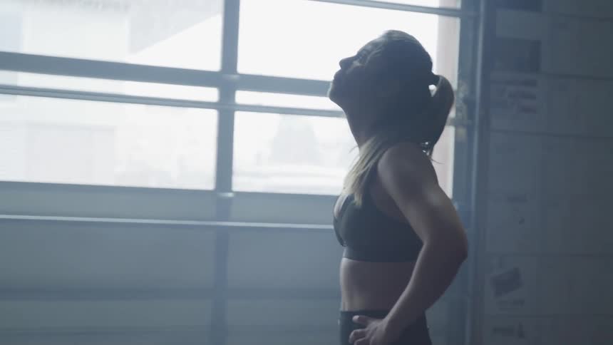 A woman stands with hands on hips as she breathes heavily and tries to catch her breath