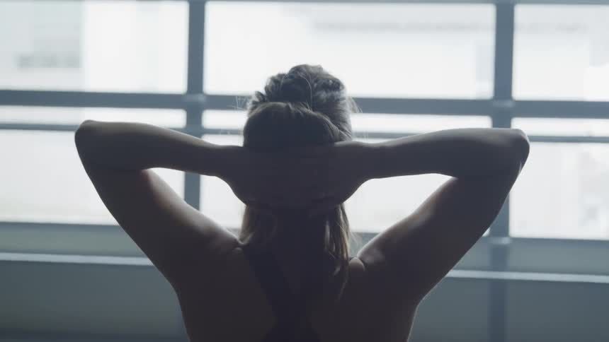 A white woman in athletic clothing looks out a window