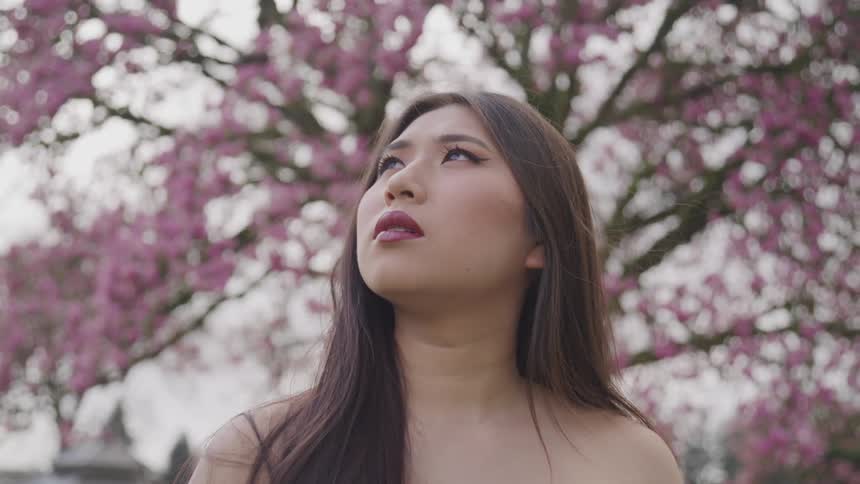 An asian woman standing beneath a redbud tree
