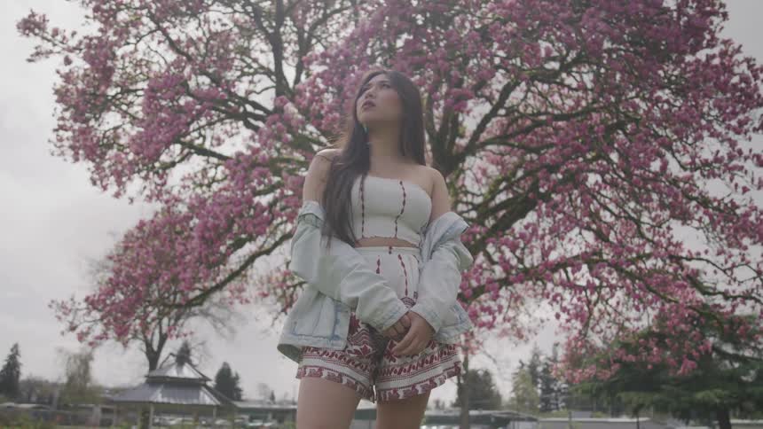 A woman staring into the sky in front of a cherry blossom tree