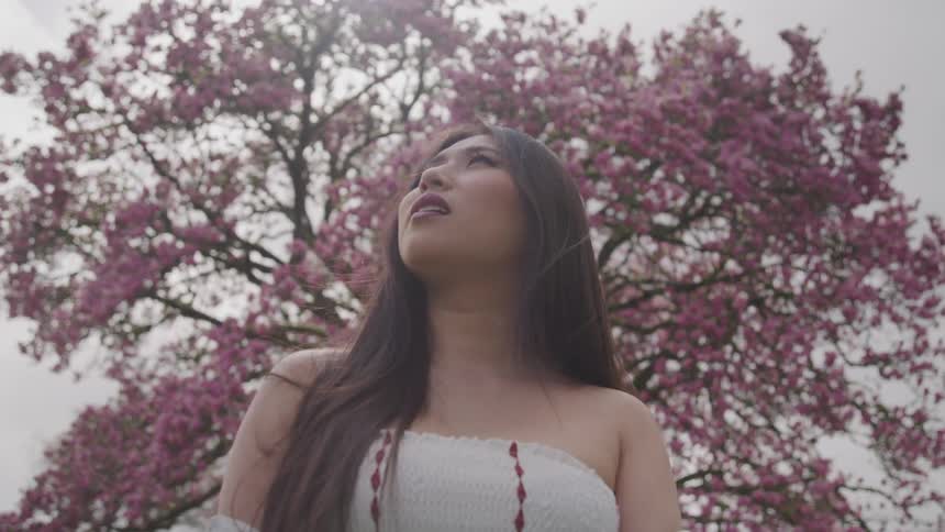 A woman looks up at the sky while standing in front of a tree with purple flowers