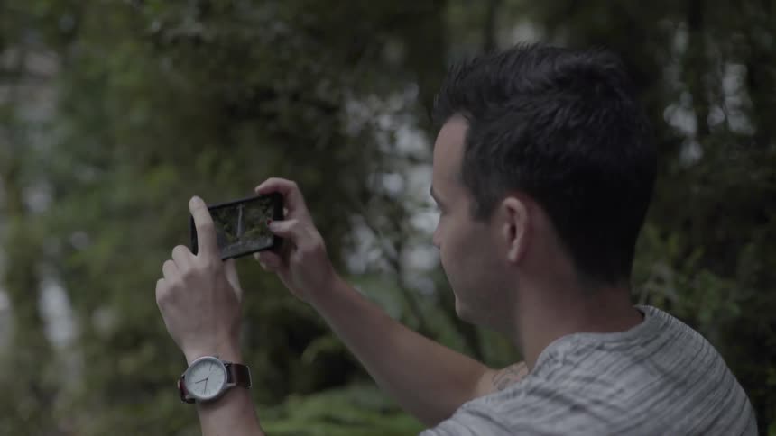 Man Using Phone to Take Photographs Outdoors Capturing Candid Moments in Natural Light.
