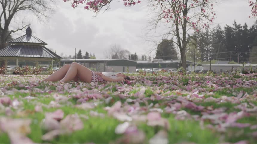 A person laying down on grass with pink flower petals