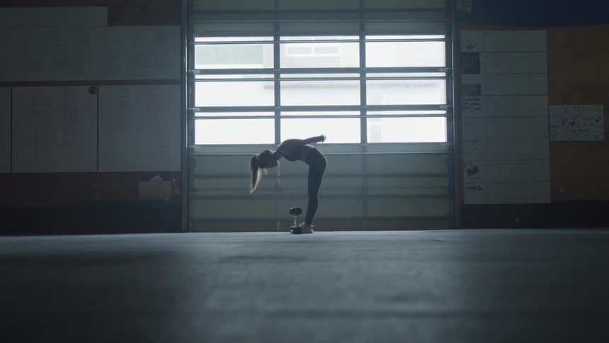 Ponytailed dancer in studio bends over and back up in front of large window