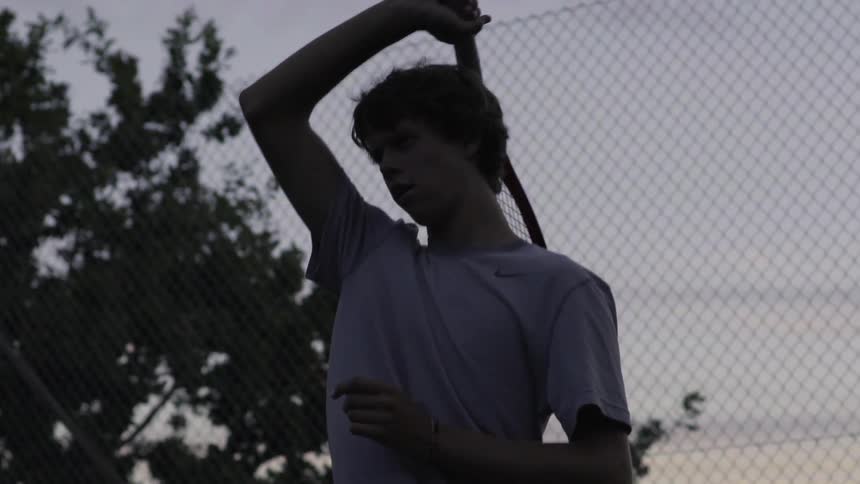 A man swings a tennis racket at sunset