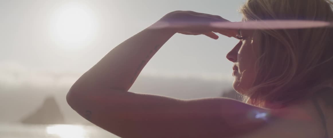 A white woman shades her eyes from the sun as she looks over the water