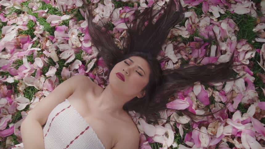 An asian woman with her hair spread out lies on a bed of flower petals
