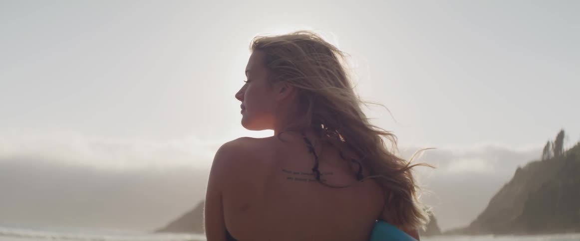 The wind blows a womans long hair around her shoulder as she looks out at the ocean