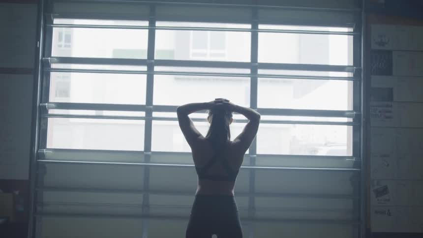 Brunette woman looks out the window and puts her hands on her head during daylight