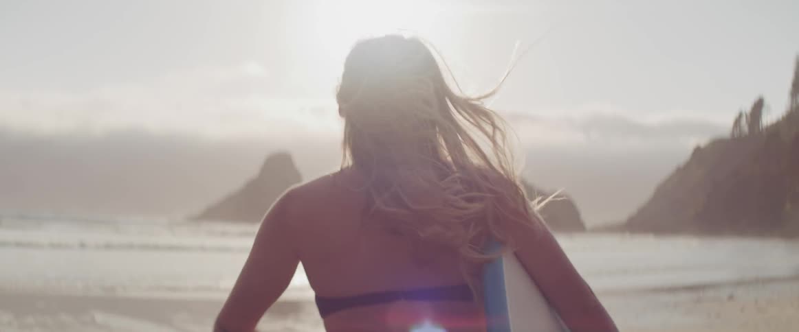 A woman is running outdoors holding a surf board