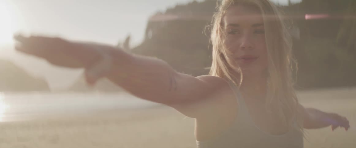 A woman holds her arms out in a yoga pose on the beach