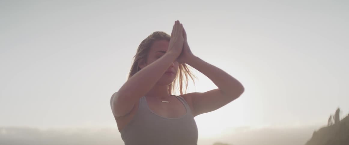 A blonde female reaches her arms overhead doing yoga outdoors at sunrise