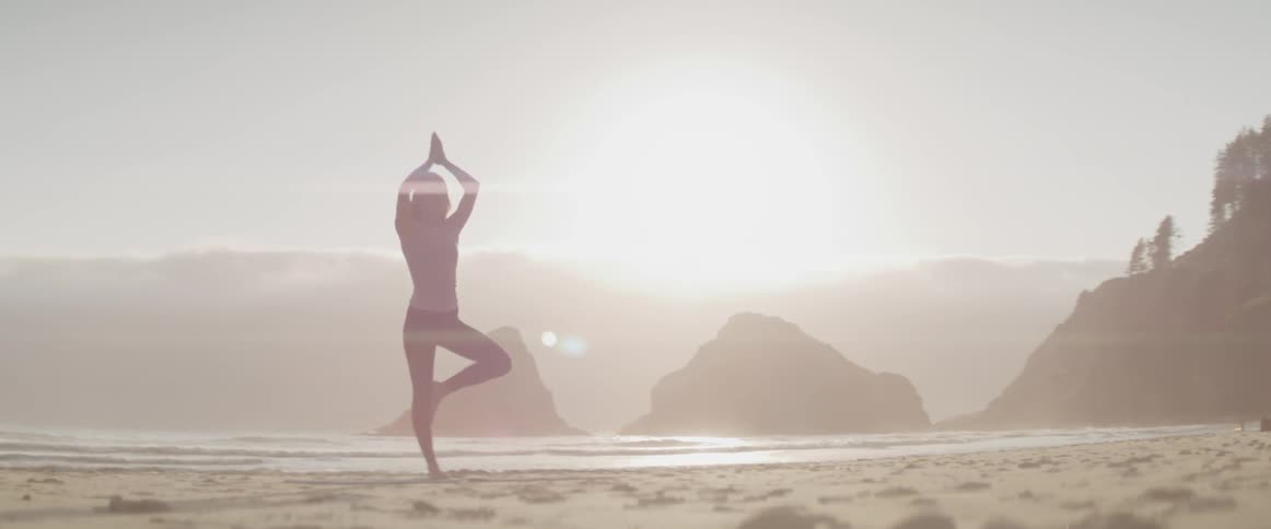 A woman doing yoga on a misty beach at sunrise