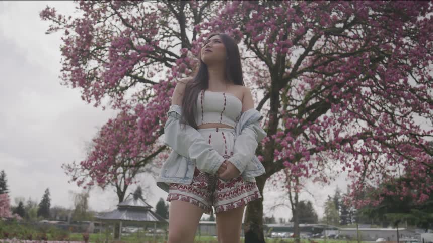 Woman stands in park under flowering tree
