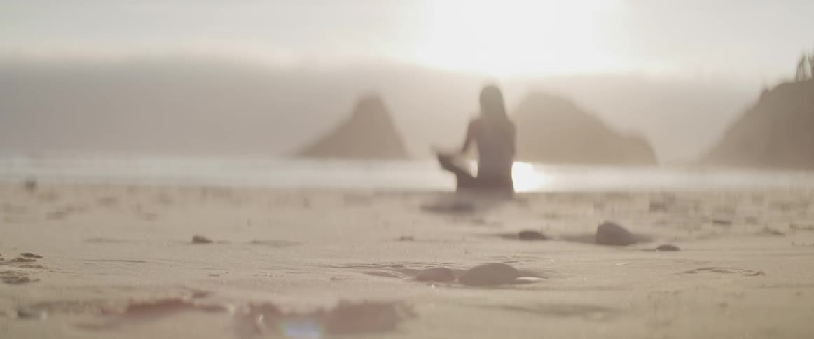 Woman sitting on beach doing yoga at sunrise