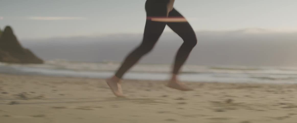 A woman in yoga pants runs barefoot on a sandy beach