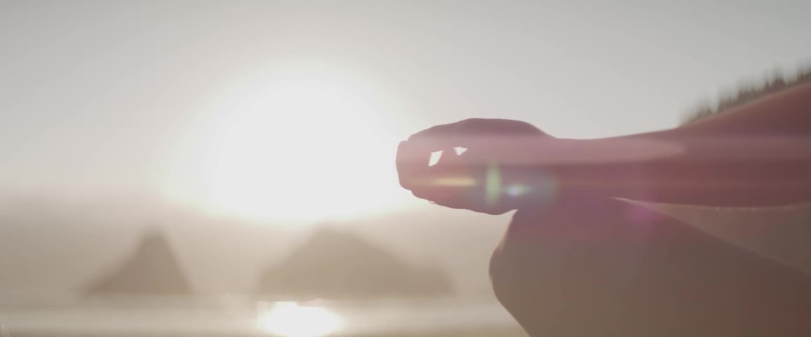 A person meditates on a beach at sunset