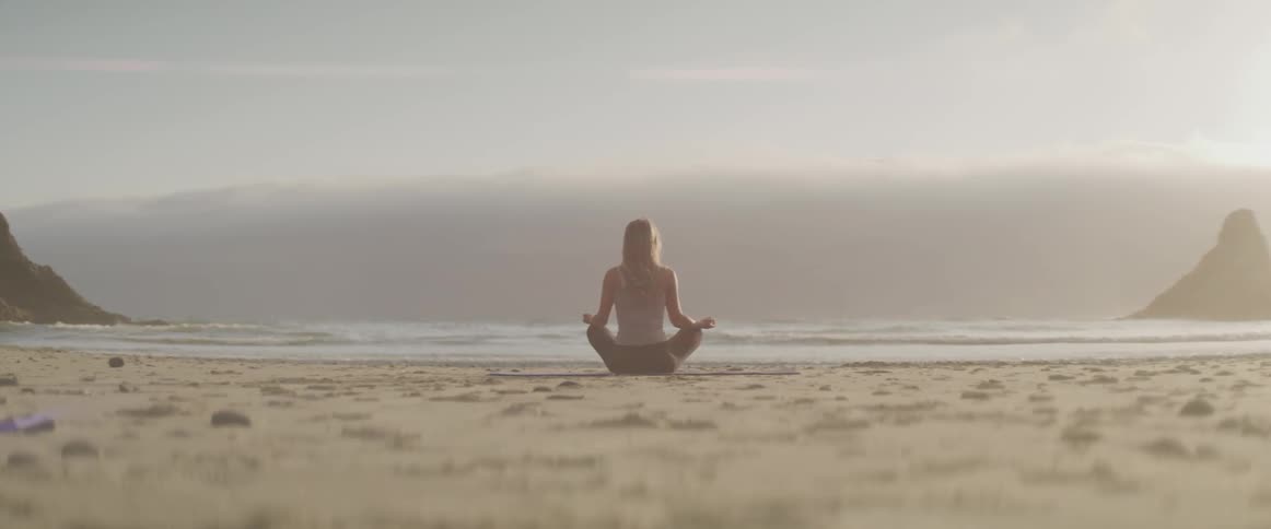 A woman sat in a relaxing position on a beach with calm rolling waves