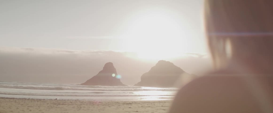 Blonde woman stands on the white sand beach and looks at sunset next to the sea