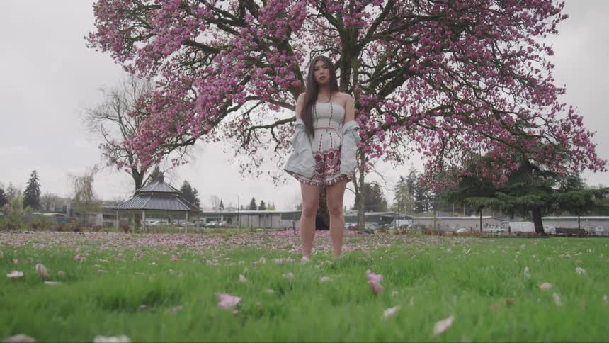 A woman is standing outdoors by a tree with flowers on it