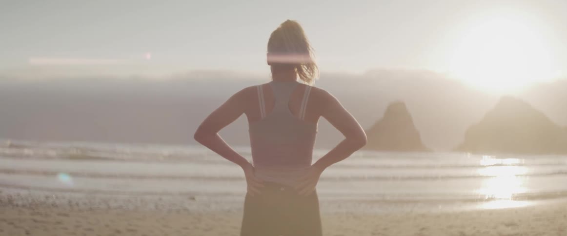 Woman standing on the beach looking at the sea at sunset