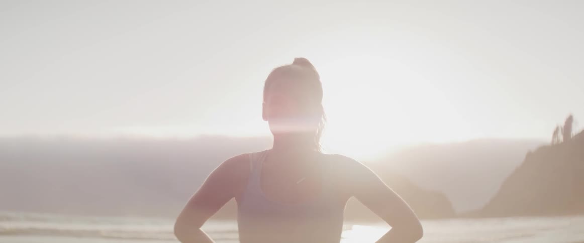 A woman stares into the camera while standing on a beach