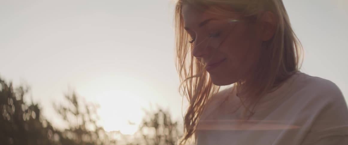 Blonde woman looks ahead and smiles while the sun goes down