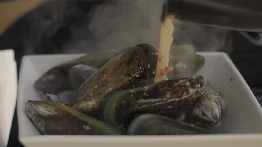 Hot liquid stock being poured over a dish of mussels