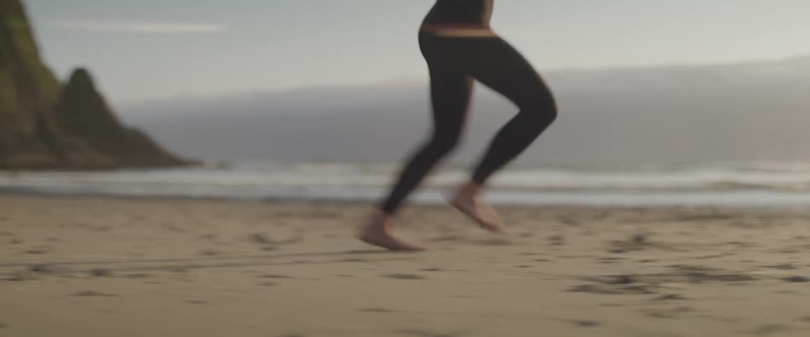 Woman wearing tights runs barefoot on the sand beach at sunset next to the sea