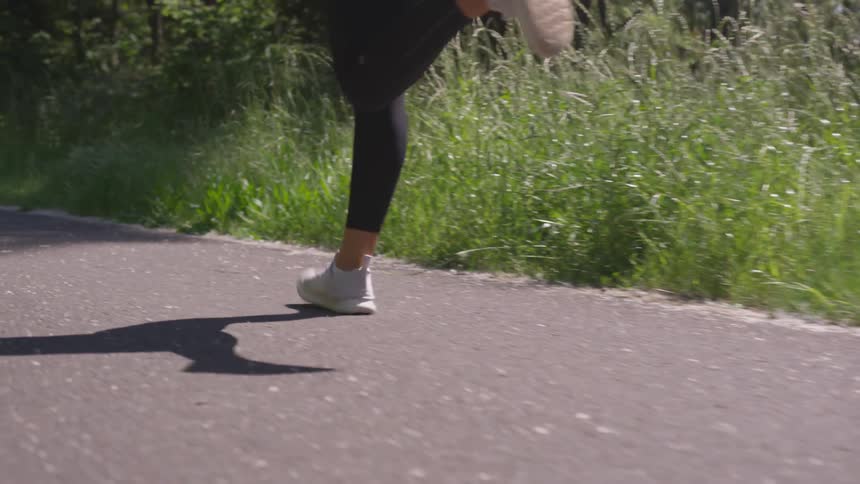 A female takes long strides while running on a paved path in a park
