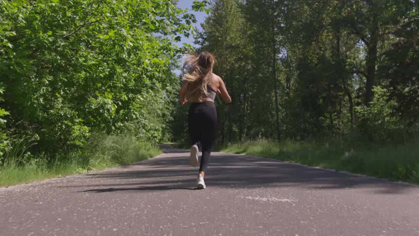 A woman is jogging outdoors in a forest area