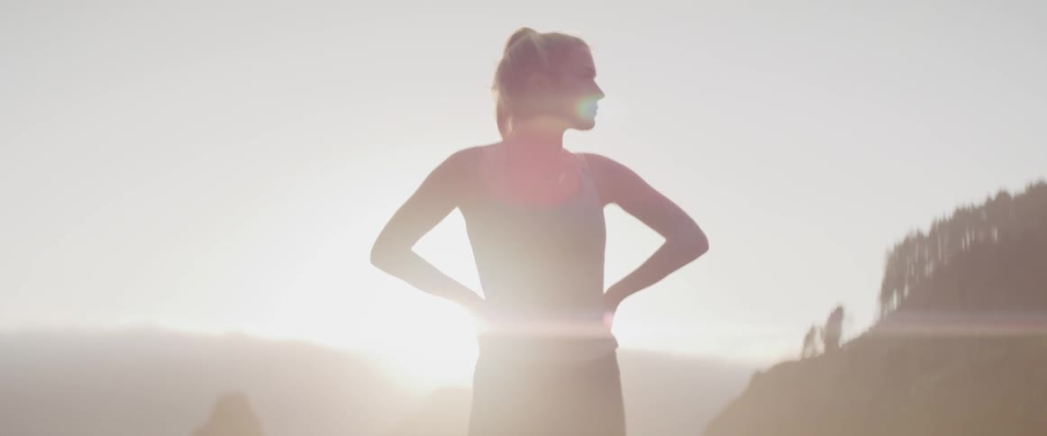 Female standing deep in thought with backdrop of sun and mountain