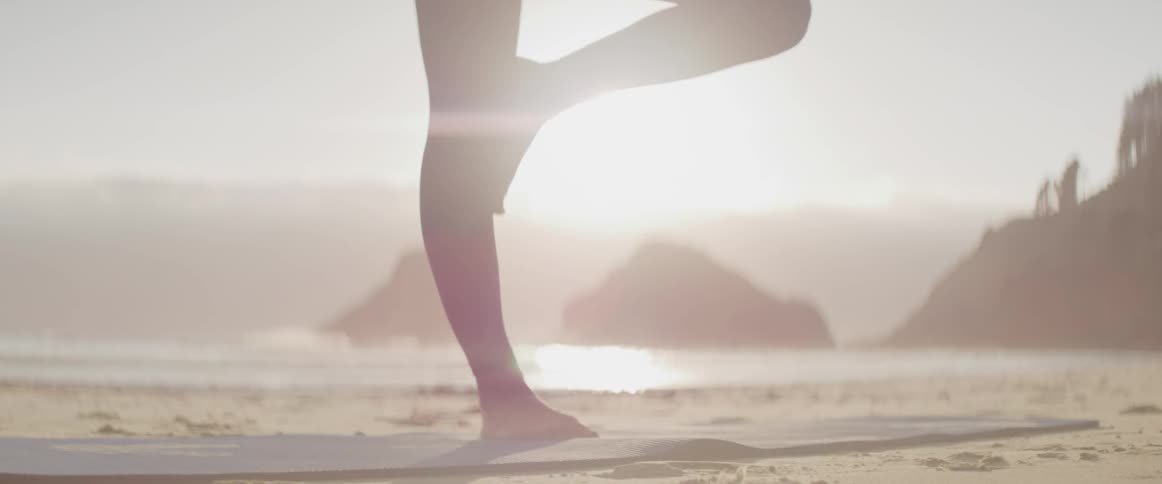 A woman is doing yoga on the sunny beach as waves gently crash behind her
