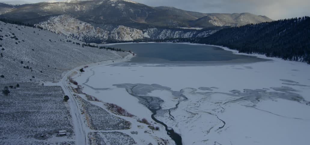 A lake covered in snow and ice with the mountains in the background