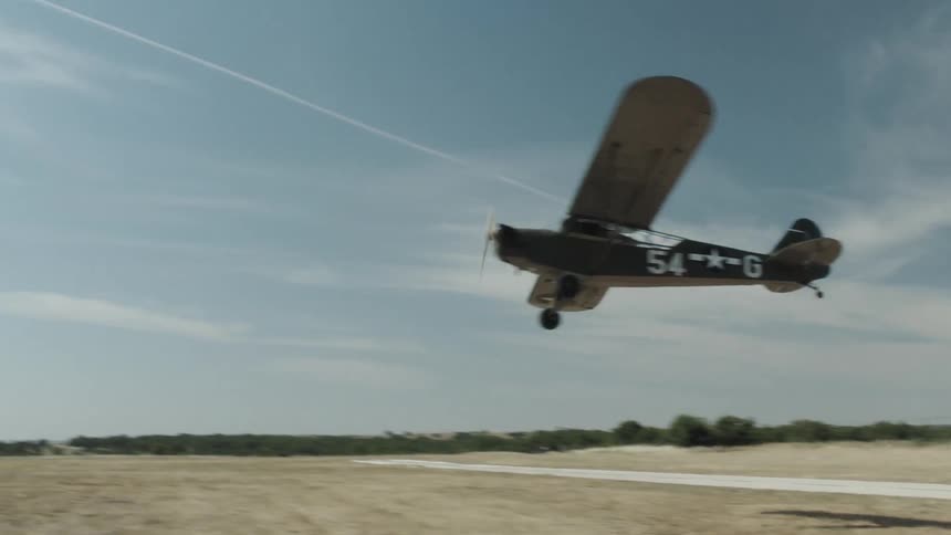 A propeller airplane flying close to the ground with the sky and clouds in the background
