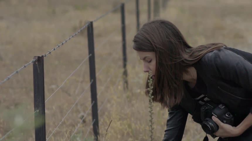 A girl is walking along a fence with a camera