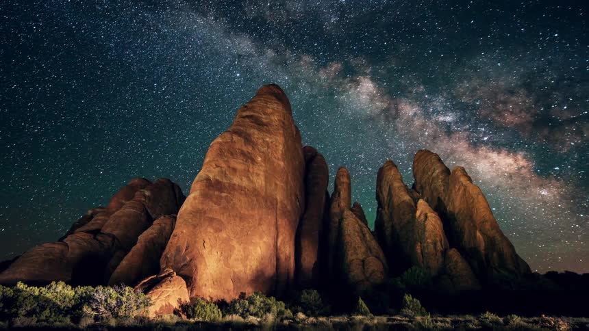 Stars pass over rock formations in a desert at night
