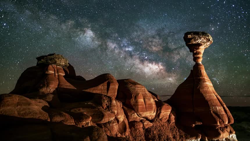 The milky way stars and lights move over desert canyon rock formations